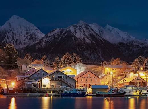 The Fisherman's Quay building lit up on the Katlian Street waterfront at night with fishing boats along the dock