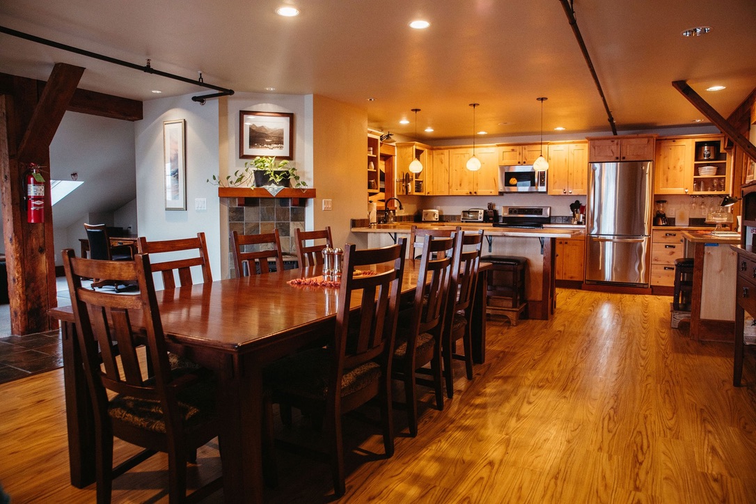 Long family style dining table set with chairs in The Loft, looking across the breakfast bar to the kitchen