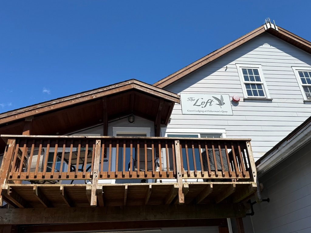 Exterior of The Loft at Fisherman's Quay showing the timber balcony and the painted Loft sign on the white gable