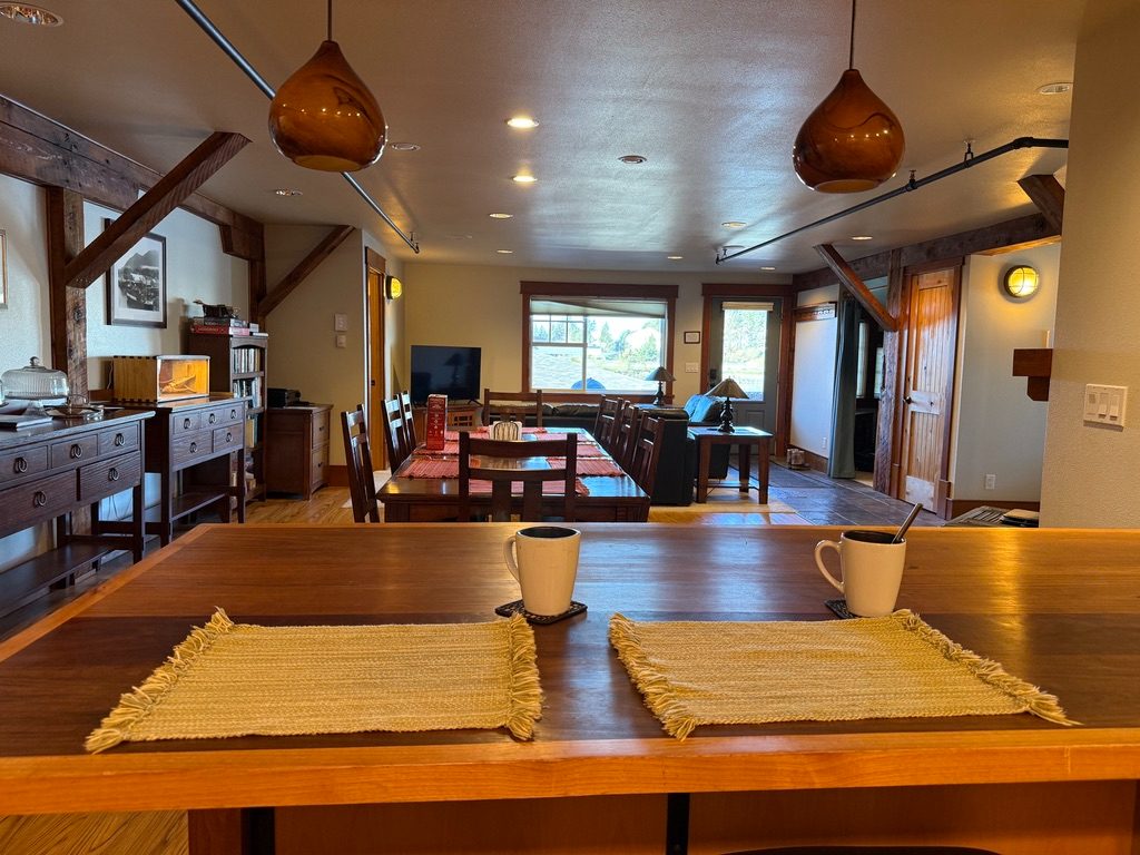 View across the breakfast bar in The Loft toward the dining table and living area, with two coffee mugs in the foreground
