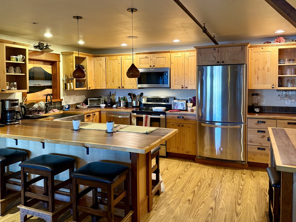 Kitchen in The Loft with knotty pine cabinets, stainless range and refrigerator, and a long wood breakfast bar with stools in the foreground