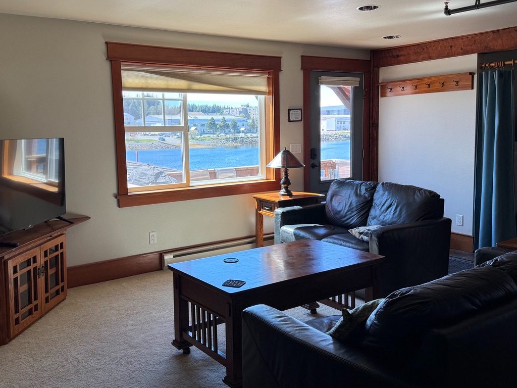 Living area in The Loft with leather sofas, television and a wide window over Sitka Channel