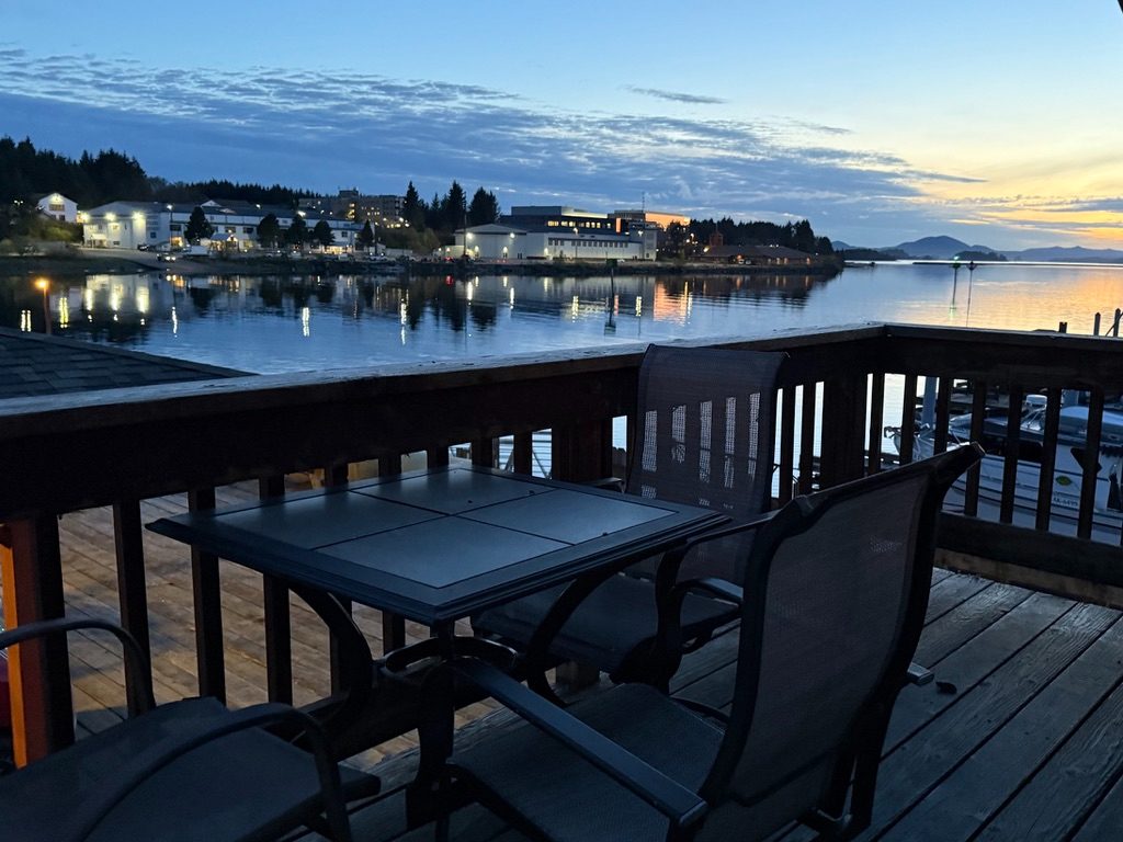 Table and chairs on The Loft's sun deck at dusk, looking across the water to the lights of Sitka