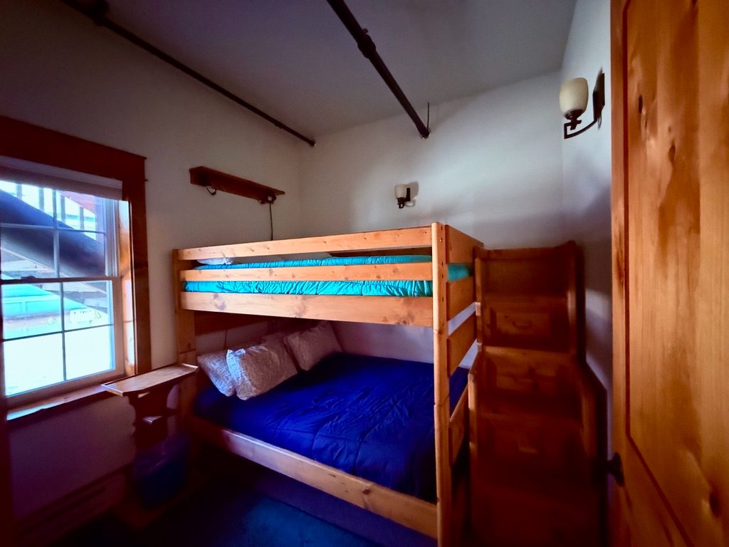 Bunk room in the North Bunkhouse with a full over full timber bunk bed beside a street-facing window