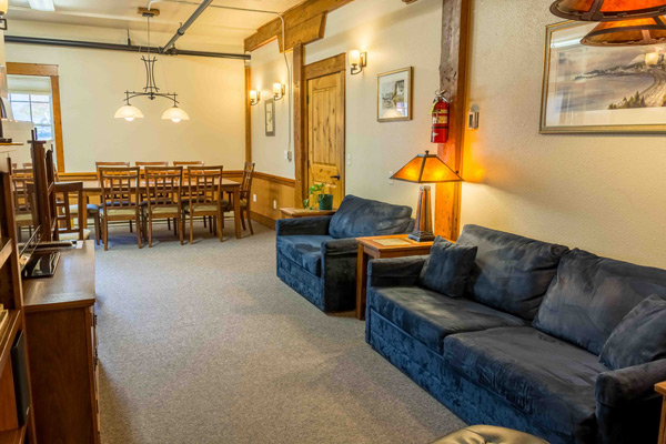 Dining table in the North Bunkhouse with blue sofas and a sitting area alongside, lit by hanging lamps