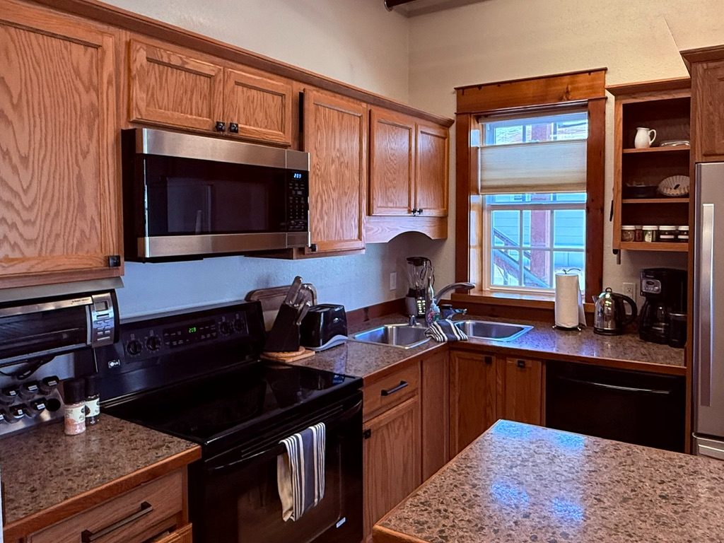 Close view of the North Bunkhouse kitchen with oak cabinets, electric range, dishwasher and a double sink under the window