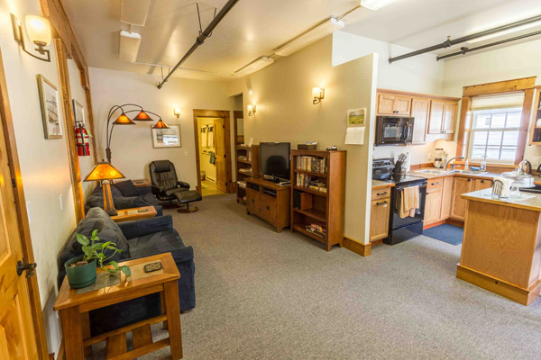 Living area of the North Bunkhouse with sofa, recliner, television and bookshelf under timber beams