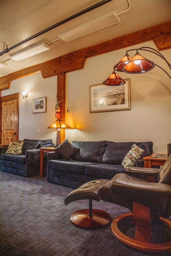 Sitting area in the North Bunkhouse with sofas, a leather recliner and an arc lamp under timber beams