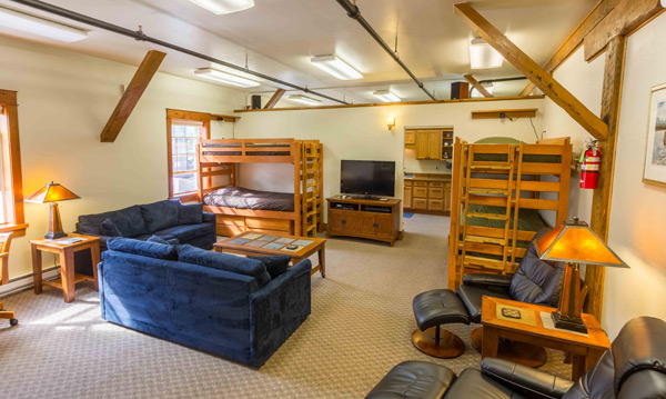 The South Bunkhouse main room with two sets of timber bunk beds, blue sectional sofas, recliners and a television