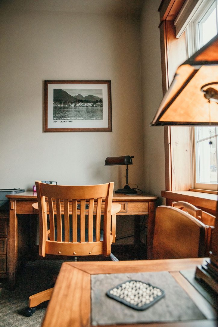 Corner desk in the South Bunkhouse with a banker's lamp and a framed historic photograph of the Sitka waterfront