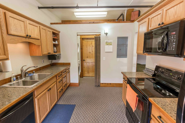 Galley kitchen in the South Bunkhouse with oak cabinets, double sink, dishwasher, electric range and microwave