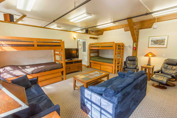 Wider view of the South Bunkhouse lounge showing bunk beds, sofas, leather recliners and exposed timber posts