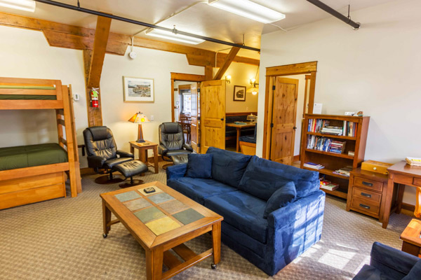 Sitting area in the South Bunkhouse with a sofa, recliners, bookshelf and desk beside the connecting door